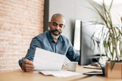 male-professional-looking-at-a-document-at-his-desk-in-an-office-setting