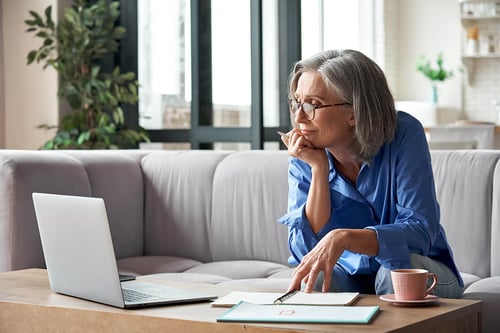 worried mature woman sitting on the couch and looking at a computer